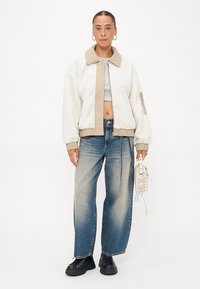 Fleece bomberjack in crème met beige accenten, voorzien van een knoopsluiting en zijzakken. Gekocht met lichtblauwe baggy jeans en zwarte laarzen.