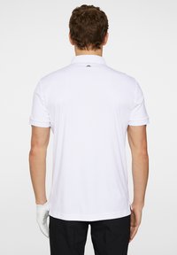 Valkoinen poolopaita klassisella kauluksella, jossa on lyhyet hihat ja suora helma. Minimalistinen muotoilu, ilman näkyviä kuvioita tai yksityiskohtia.