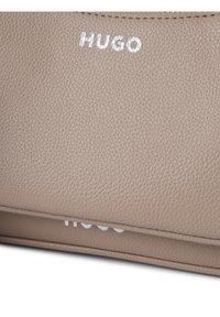 Beige Lederhandtasche mit strukturiertem Oberflächenfinish. "HUGO" in Silber nahe der Oberkante geprägt. Minimalistisches Design mit klaren Linien.