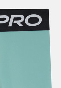 Un gros plan sur des shorts de compression vert menthe clair avec une ceinture élastique noire arborant le texte blanc "PRO" bien en vue.