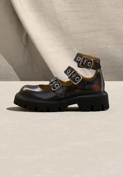 Χοντρό μαύρο δερμάτινο παπούτσι με παχιά λαστιχένια σόλα και τρεις ασημένιες αγκράφες πάνω από το πάνω μέρος και τον αστράγαλο.