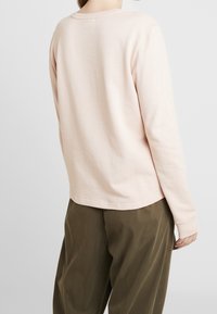 Jasnoróżowa koszula z długim rękawem z miękkiego bawełnianego materiału, z okrągłym dekoltem i luźnym krojem, w połączeniu z oliwkowymi spodniami.