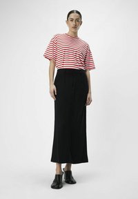 Chemise à rayures rouges et blanches à manches courtes, jupe longue noire, chaussures noires à enfiler. Tissu lisse, coupe décontractée, design minimaliste.