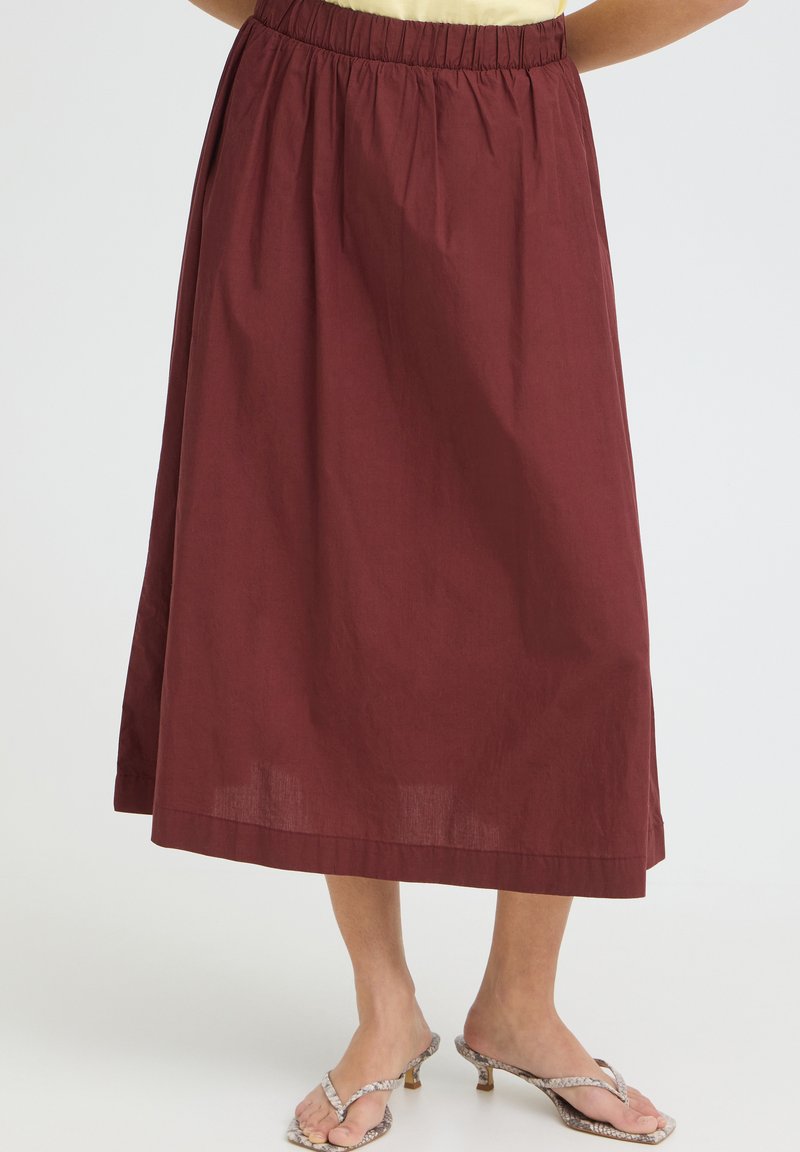 Femme portant une jupe bordeaux mi-longue et ample avec une ceinture élastique, ainsi que des sandales à talons beiges avec un motif peau de serpent.