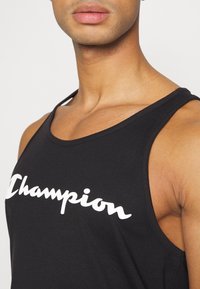 Top sin mangas negro de algodón, con un logo blanco de "Champion". Corte con amplios agujeros para los brazos y un escote redondeado. Textura suave.