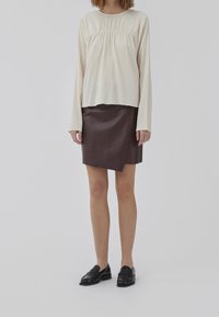 Krämfärgad, texturerad långärmad topp matchad med en brun, konstläder, insvept kjol. Svarta loafers fulländar looken. Enkel, modern design.