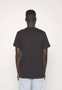 Svart kortärmad t-shirt i bomull med rund halsringning. Slät textur och avslappnad passform, sedd bakifrån. Oprydlig design utan dekorationer.