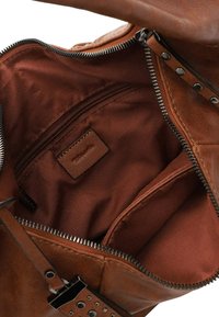 Sac en cuir marron avec une fermeture éclair métallique ouverte montrant l'intérieur en tissu marron, une poche zippée et une petite étiquette en cuir cousue à l'intérieur.