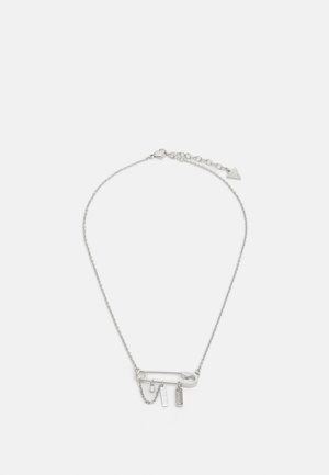 Silver chain necklace with a large safety pin pendant holding charms including a small chain, crystal, and "GUESS" tag.