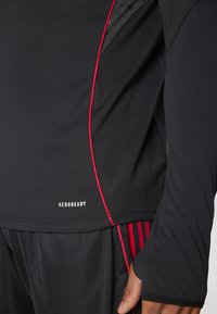 Black athletic long-sleeve top featuring red accents, smooth texture, and AEROREADY branding at the hem. Designed for comfort and performance.