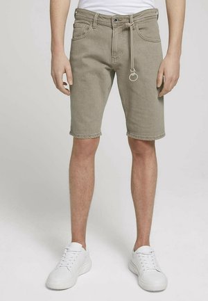 Beige denim shorts, knee-length, featuring a drawstring waist with a metal ring. Worn with white sneakers, plain white t-shirt above.