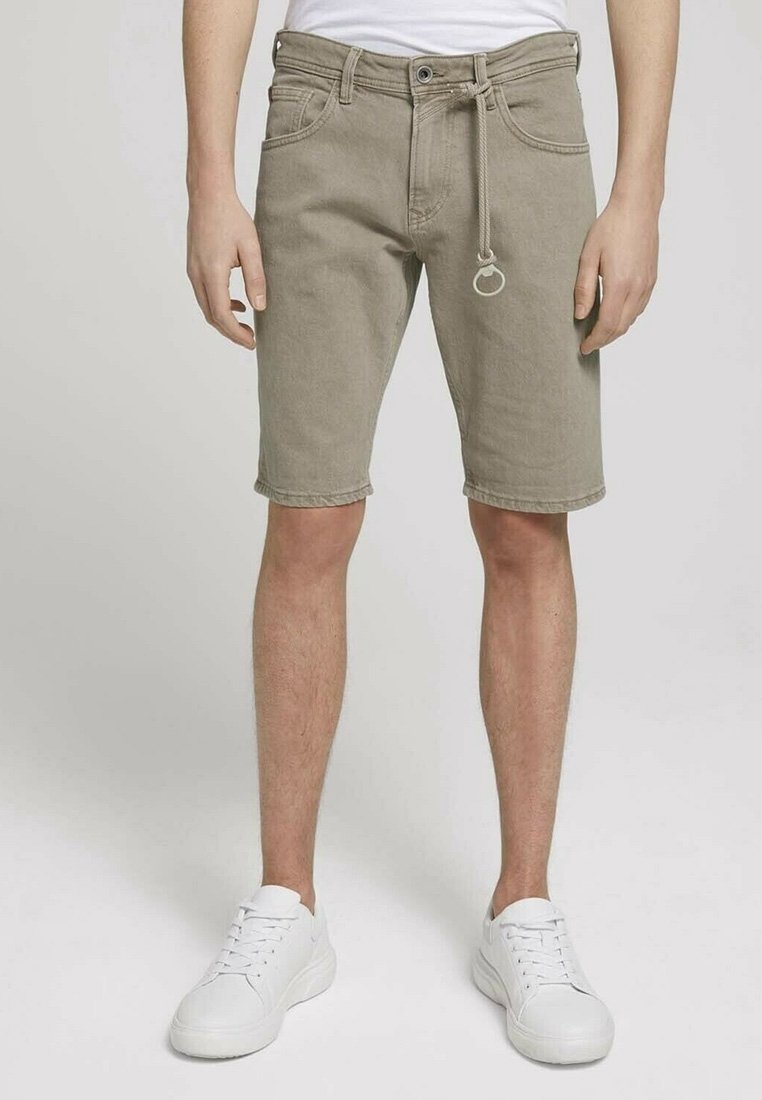 Shorts en denim beige, longueur genoux, avec une taille à cordon et un anneau en métal. Portés avec des baskets blanches et un t-shirt blanc uni.