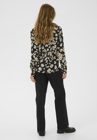 Zwarte blouse met lange mouwen en een crèmekleurig bloemenpatroon, gecombineerd met zwarte broeken en chunky zwarte schoenen, met een ontspannen pasvorm en een zachte textuur.
