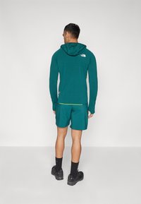 Haut à capuche à manches longues teal et shorts assortis. Le haut présente un logo dans le dos, tandis que les shorts ont une coupe décontractée et des poches latérales.