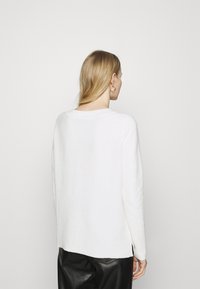 Biały sweter z długim rękawem w luźnym fasonie, o prążkowanej fakturze, okrągłym dekolcie i bocznych slits, zestawiony z czarnymi skórzanymi spodniami.