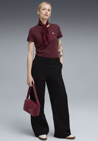 Maron farvet t-shirt med et lille logo, sorte brede bukser og en rød quiltet håndtaske. Modellen har en rød leopardmønstret tørklæde og cremefarvede sko på.