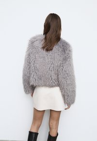 Fluffy grå sweater med cropped design, lange ærmer og en tekstureret finish, kombineret med en kort cremefarvet nederdel og sorte knælange støvler.