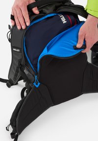 Sac à dos en millet noir avec intérieur bleu et marine. La fermeture éclair ouverte révèle des compartiments rembourrés avec des textures contrastantes et une tirette bleu.