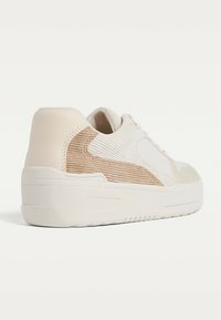 Sneaker con una combinazione di colori crema e beige, caratterizzato da un mix di pelle liscia e tessuti a coste. Suola bianca spessa e design con lacci.