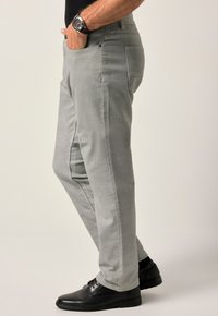 Grå byxor i strukturerad tyg, med sidofickor, åtsittande passform och i kombination med svarta skor. Slät yta och diskret design.