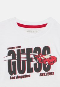 Λευκό βαμβακερό μπλουζάκι με κόκκινο γιακά, έντονο μαύρο κείμενο "GUESS" με γραφικό κόκκινο αγωνιστικό αυτοκίνητο και τη φράση "RACING TEAM Los Angeles EST.1981."