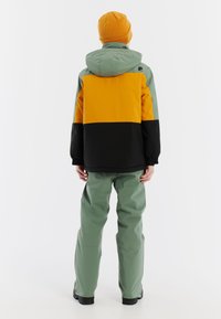 Waterdichte jas en broek set heeft een kleurblokontwerp in geel, groen en zwart. De jas heeft een capuchon en elastische manchetten.