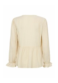 Blusa a maniche lunghe color crema con tessuto testurizzato. Presenta una vita arricciata e polsini con volant accentuati da piccole perle.