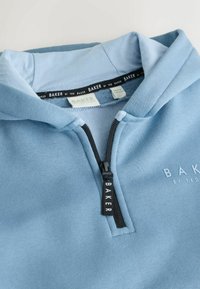 Blauer Sweatshirt mit Reißverschluss aus weichem Stoff. Hat einen schwarzen Reißverschluss mit "BAKER"-Etikett und ein kleines gedrucktes Logo. Einfaches Kapuzendesign.