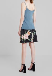 Ljusblå tanktopp med tunna band, kombinerad med en svart blommönstrad kjol med rosa blommor och gröna blad. Svarta klackar med ankelrem.