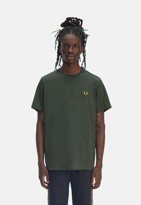 Camiseta de manga corta verde oscuro hecha de algodón, con un pequeño logo dorado en el pecho y un corte relajado. Textura suave, cuello redondo clásico.