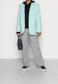Máta zelený oversized blazer, černou mikinu s kapucí, světle šedé široké kalhoty, námořnickou kabelku se zlatými akcenty a námořnické tenisky.