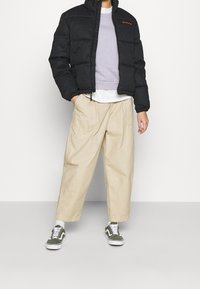 Doudoune noire, sweat-shirt gris, pantalon crème et baskets vertes. Tissu texturé avec fermeture éclair et poignets élastiques. Tenue décontractée.