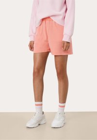 Bermuda in corduroy rosa con una vestibilità comoda e una cintura elastica, abbinate a sneakers bianche e calzini rigati nei toni pastello.