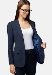 Granatowa marynarka wykonana z teksturowanej tkaniny, z klapami i dwoma przednimi kieszeniami. Wewnątrz widoczna jasnoniebieska podszewka w wzory.