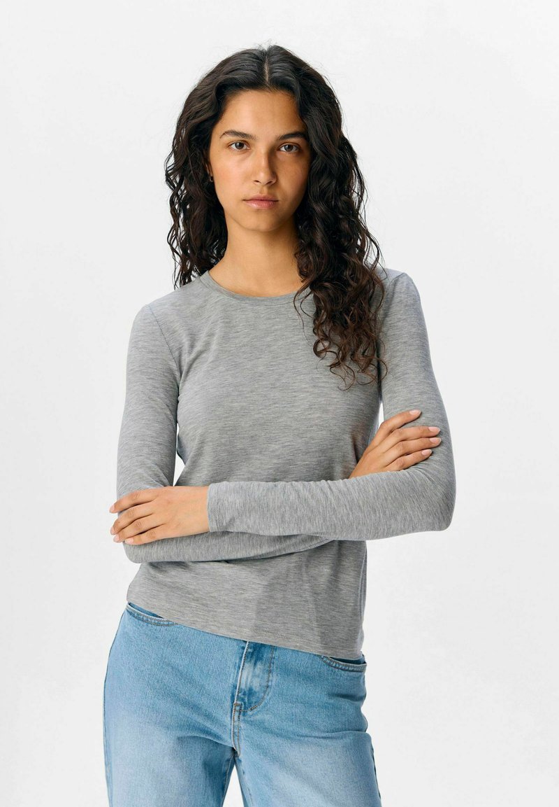 Grå langærmet skjorte lavet af et blødt, glat stof. Har rund halsudskæring og tætsiddende ærmer, parret med lyseblå denimjeans.