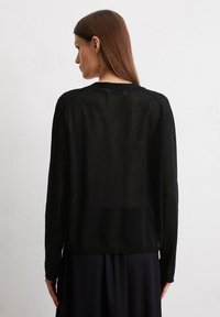 Schwarzer, leichter Pullover mit einer weichen, durchsichtigen Textur. Verfügt über lange Ärmel, einen runden Ausschnitt und einen geraden Schnitt, von hinten betrachtet.