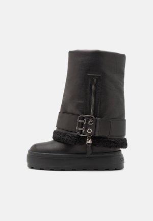 Černá kožená bota s vysokým holenním dílem, boční zip a texturovaný černý kožešinový lem. Obsahuje pásek s detailním přezkou a silnou podrážku.