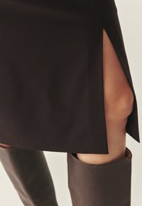 Falda negra con una abertura lateral, combinada con botas de cuero marrón hasta la rodilla. Textura suave con un ajuste entallado.