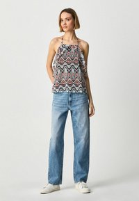 Top de halter de colores multicolores con detalles de volantes, combinado con jeans de tiro alto azul claro y zapatillas blancas.