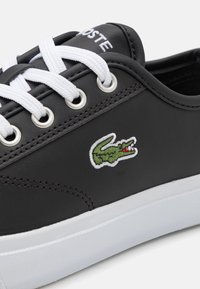 Fekete szintetikus sneaker fehér fűzőkkel, fém szemállásokkal és zöld hímzett krokodil logóval. Fehér gumitalp.