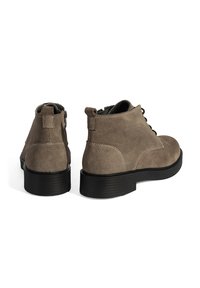 Braune Wildleder-Stiefeletten mit runder Zehenpartie, Schnürung vorne und schwarzer Gummisohle. Mit gestickten Akzenten und Schlaufen an der Rückseite.