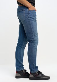 Blå denimjeans med rak passform, som har fem fickor och ett subtilt sömnadsmönster. Bärs med svarta och grå sneakers.