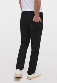 Jeans de mezclilla negra con corte recto, que cuentan con bolsillos traseros y detalles de costura sutiles. Combinados con zapatillas blancas.