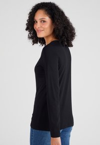 Zwarte langemouwen shirt van zacht katoen, met een ronde hals en een relaxed fit. Model poseert iets zijwaarts.