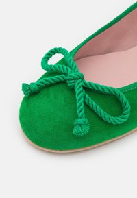 Ballerine en daim vert avec un nœud en corde torsadée sur l'avant arrondi et une doublure intérieure rose clair.