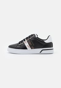 Sneakers en cuir noir avec une bande blanche et à motifs, accents dorés, bout arrondi, lacets noirs et semelle en caoutchouc blanche.