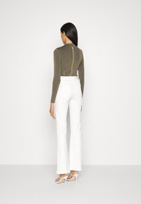 Top verde măsliniu cu mâneci lungi, cu fermoar la spate, asociat cu pantaloni albi evazați cu talie înaltă și sandale cu toc transparent.