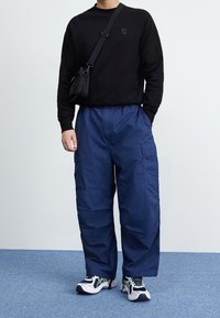 Musta collegepaita, jossa pieni logo, yhdistetty tummansinisiin cargo-housuihin, joissa on sivutaskut. Kokonaisuuden täydentävät valkoiset ja tummansiniset lenkkarit.