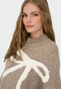 Pull en tricot taupe avec un motif abstrait blanc, doté d'un col montant côtelé et d'une coupe ample texturée.