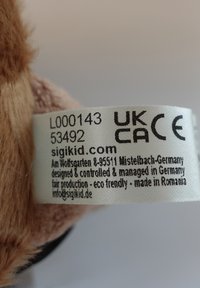 Label on plush toy showing UKCA and CE marks, model number L000143, made in Romania, designed and managed in Germany, website sigikid.com.